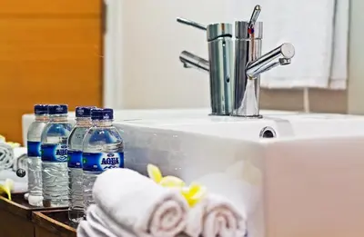 a bathroom sink with bottles of water and towels at Sunset Residence and Condotel in Legian