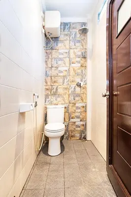 a bathroom with a toilet and a stone wall at Puri Agung Homestay in Kuta