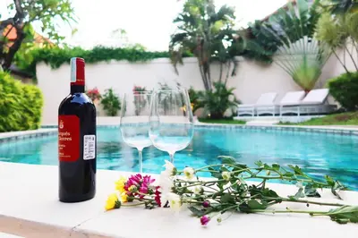 a bottle of wine and two glasses on a table by a pool at Villa Coconut Bali in Seminyak