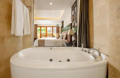 a bath tub in a bathroom with a bedroom at Villa Kayu Raja in Seminyak