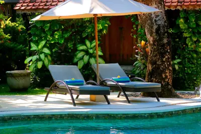 two chairs and an umbrella next to a pool at Pearl Boutique Hotel Adult only in Legian