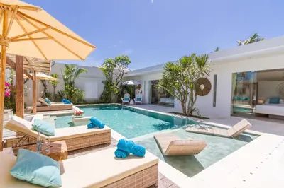 a swimming pool with chairs and an umbrella at Villa Smilla in Seminyak