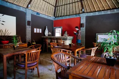 a restaurant with wooden tables and chairs and a person in the background at Ellies Hotel in Nusa Dua