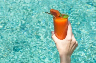 a hand holding a orange cocktail in front of a pool at Villa Air Bali Boutique Resort and Spa in Seminyak