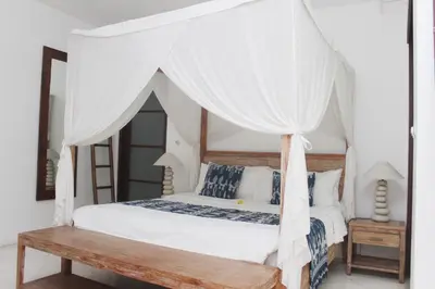 a bedroom with a white canopy bed with a wooden bench at Villa Sahaja in Canggu