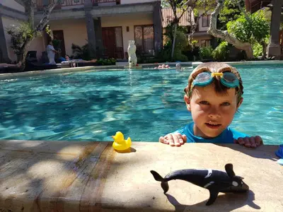 a young child wearing goggles and a toy shark in a swimming pool at Puri Mesari Hotel in Sanur