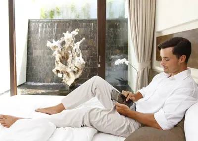 a man sitting on a bed looking at a tablet at eqUILIBRIA Seminyak in Seminyak