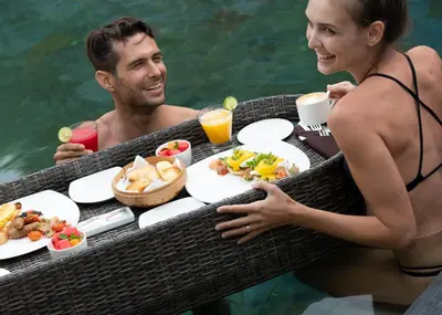 a man and woman in the water with a tray of food at eqUILIBRIA Seminyak in Seminyak