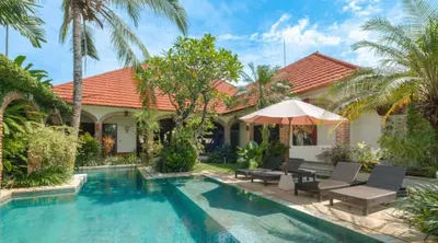 a house with a swimming pool with chairs and an umbrella at Bali Dyana Villas in Seminyak