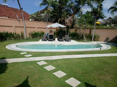 a pool with chairs and an umbrella in a yard at Bali Dyana Villas in Seminyak