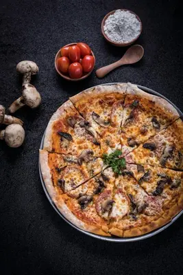a pizza sitting on a table with tomatoes and mushrooms at The Banyumas Villa in Denpasar