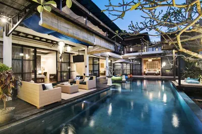 an indoor pool with white furniture and a house at Sunset Paradise at Temple Hill Jimbaran in Jimbaran