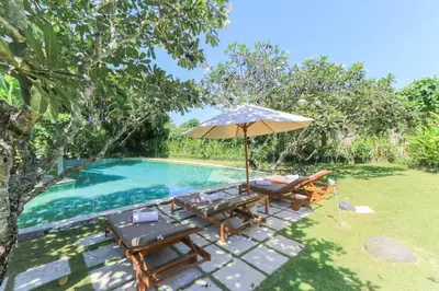 an umbrella and chairs next to a swimming pool at Villas Sin Sin in Canggu