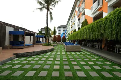 a courtyard with green grass and buildings and palm trees at Bliss Surfer Hotel Legian in Legian