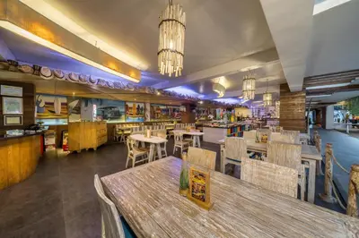 a restaurant with wooden tables and chairs and a kitchen at Bliss Surfer Hotel Legian in Legian