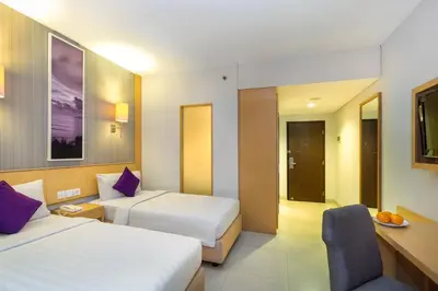 a hotel room with two beds and a chair at Quest Hotel Kuta by ASTON in Kuta