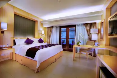 a hotel room with a large bed and a desk at Quest Hotel Kuta by ASTON in Kuta