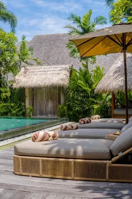 a row of lounge chairs with an umbrella and a pool at Space Villas Bali in Seminyak