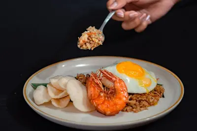 a person eating a plate of food with an egg and shrimp at Bali Summer Hotel by Amerta in Kuta