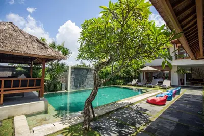 a pool with a tree next to a house at Amore Villas in Canggu