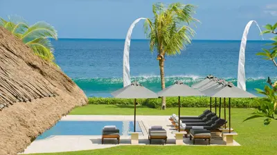 a group of chairs and umbrellas next to the ocean at Villa Atas Ombak in Seminyak
