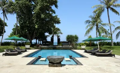 a swimming pool with chairs and a fountain and palm trees at Villas at The Patra Bali Resort and Villas - CHSE Certified in Kuta