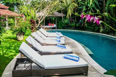 a group of lounge chairs next to a swimming pool at Villa Sipo in Seminyak