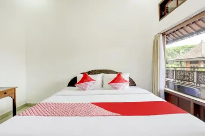 a bedroom with a bed with red pillows and a window at Hotel O Ratu in Denpasar