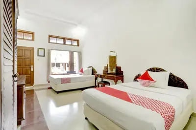 a bedroom with two beds and a desk and a window at Hotel O Ratu in Denpasar