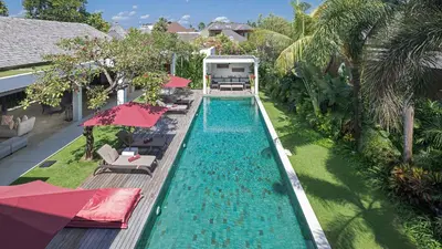 a swimming pool with chairs and umbrellas next to a house at Casa Brio in Seminyak