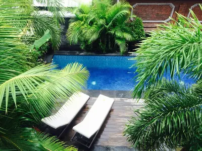a pool with two white benches and palm trees at Tanjung Sari Inn in Nusa Dua