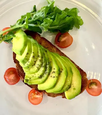 a white plate with a sandwich with avocado and lettuce at Villa Ria Bali in Seminyak
