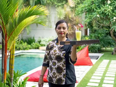 a woman holding a tray with a drink on it at Villa Arte by Villa Finder in Seminyak