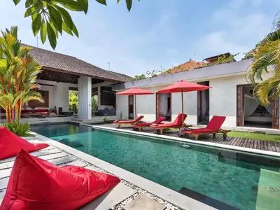 a pool with red chairs and umbrellas next to a house at Villa Arte by Villa Finder in Seminyak