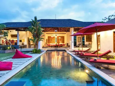 a pool with chairs and umbrellas in front of a house at Villa Arte by Villa Finder in Seminyak