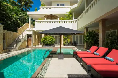 a pool with red chairs and an umbrella next to a house at Beach Melati Apartments in Legian