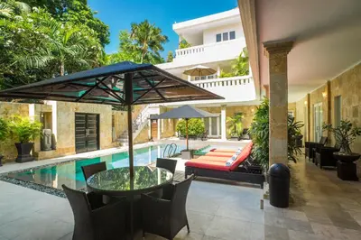 an outdoor patio with a table with an umbrella and a pool at Beach Melati Apartments in Legian