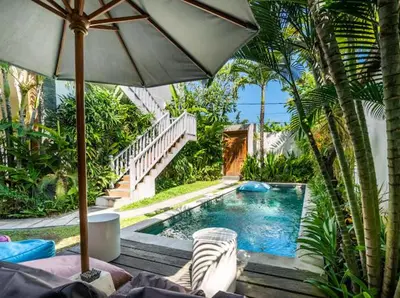 a swimming pool with an umbrella and some palm trees at Kubu Guest House in Seminyak