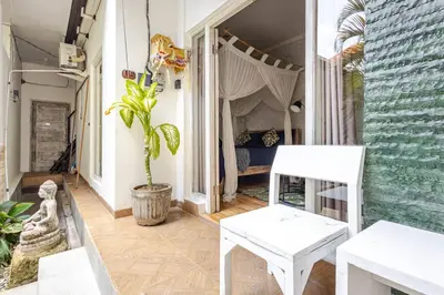 a porch with two white chairs and a bed at Kubu Guest House in Seminyak