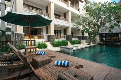 a resort with a swimming pool with chairs and an umbrella at Fourteen Roses Beach Hotel in Legian