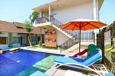 a pool with a chair and an umbrella next to a house at Lembayung Sari Homestay in Denpasar