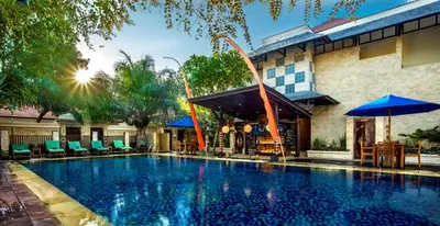 a swimming pool with chairs and umbrellas next to a building at Best Western Kuta Villa in Kuta