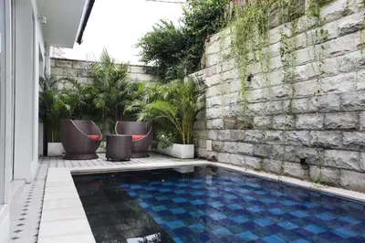 a swimming pool in front of a brick wall with plants at Villa Marronniers in Seminyak