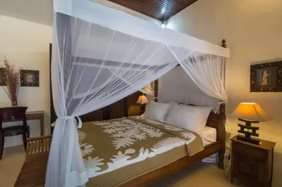 a bedroom with a bed with a canopy and a desk at Villa Kamboja Senior in Legian