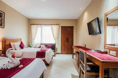 a hotel room with two beds and a desk at Kuta Puri Bungalows, Villas and Resort in Kuta