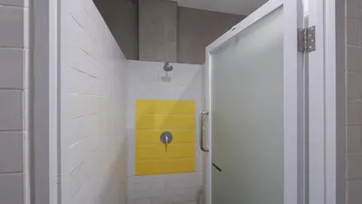 a bathroom with a shower with a yellow wall at Beach Hut Hostel in Kuta