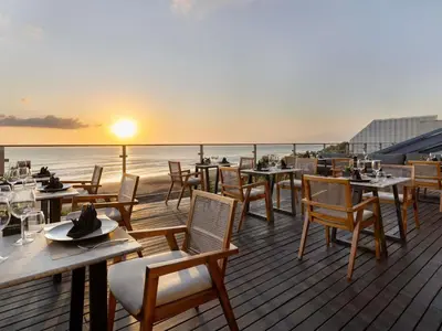 a deck with tables and chairs and the ocean at sunset at Grand Seminyak Lifestyle Boutique Bali Resort in Seminyak