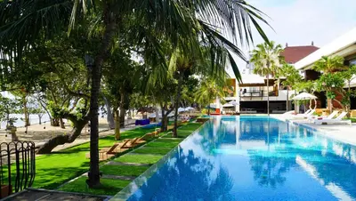 a swimming pool with palm trees and a building at Truntum Kuta Bali in Kuta