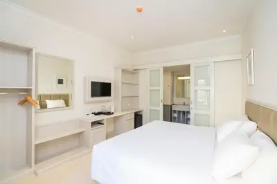 a white bedroom with a bed and a desk at Alron Hotel Kuta in Kuta