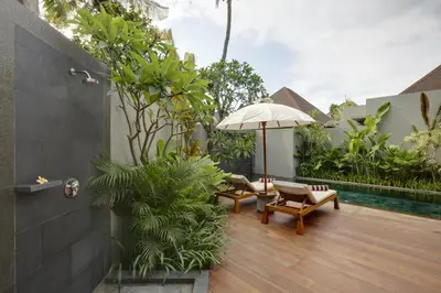 a patio with chairs and an umbrella and a pool at KoenoKoeni Villa in Seminyak